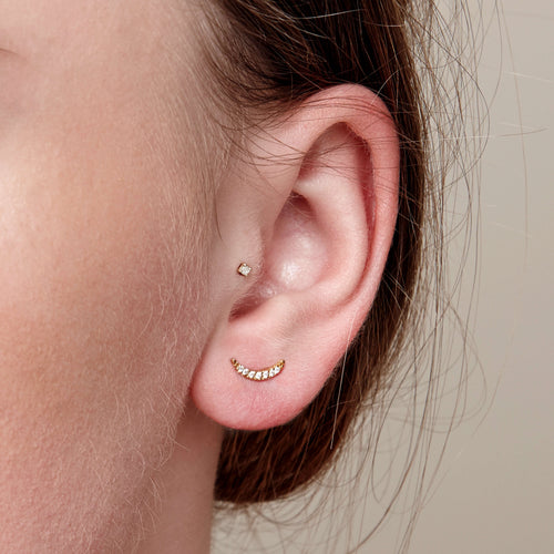 The gold crescent stud is worn by a young model in the first piercing.