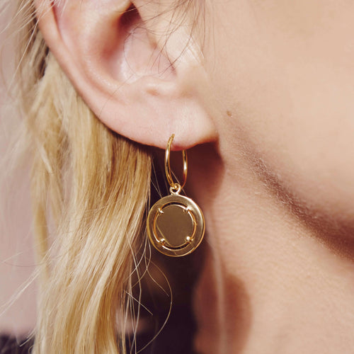 an ear with a gold hoop earring in with a gold coin pendant handing from he hoop